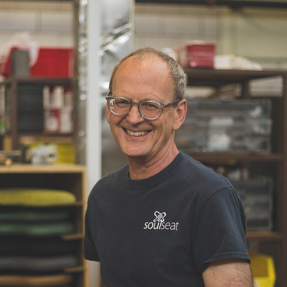 photo of man smiling at the camera in a soul seat shirt with a stack of colorful soul seat cushions behind him
