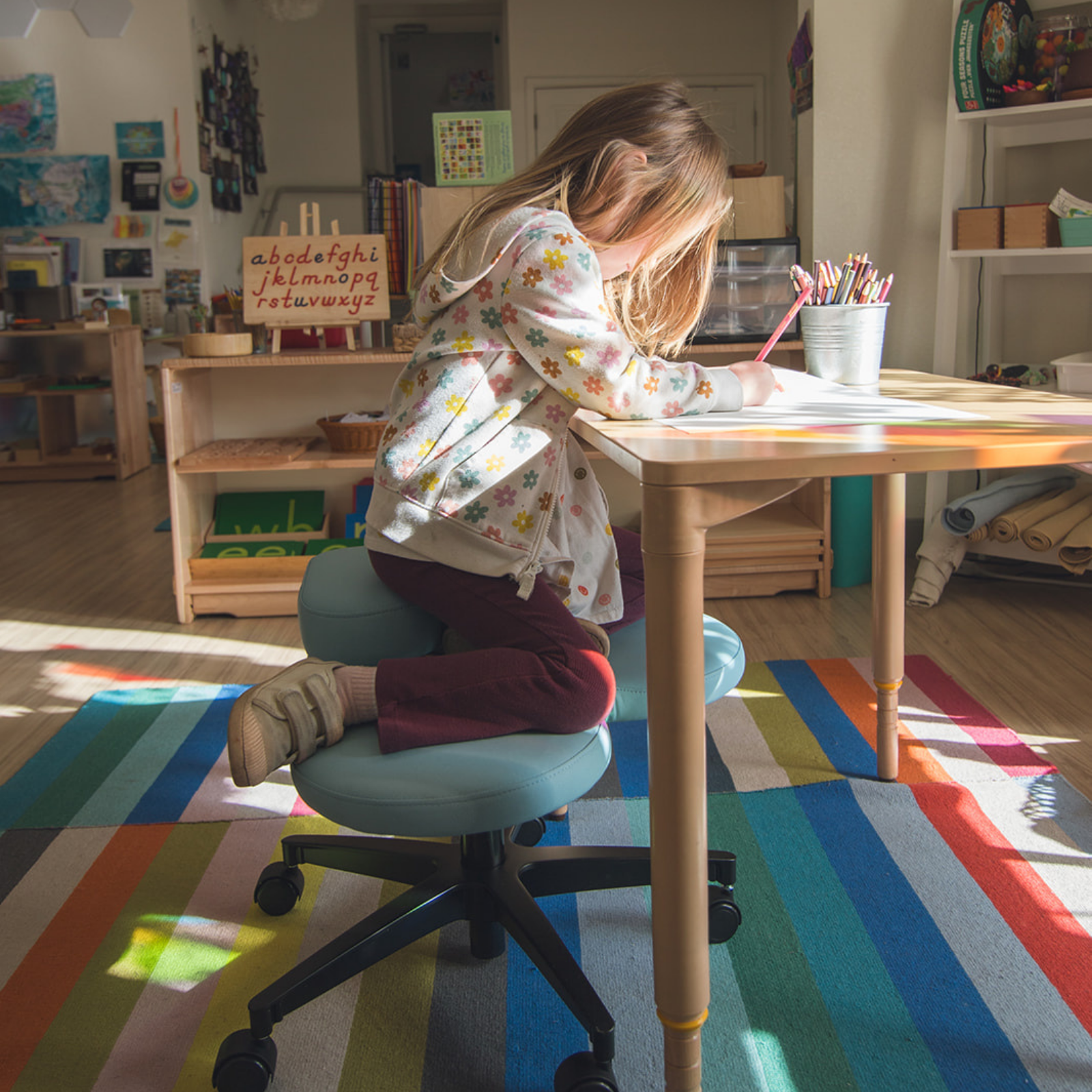 child sitting on blue fidget seat in a classroom on a colorful rug