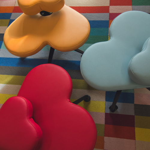 Three fidget seats in red, orange, and light blue, arranged on a colorful striped and checkered rug.
