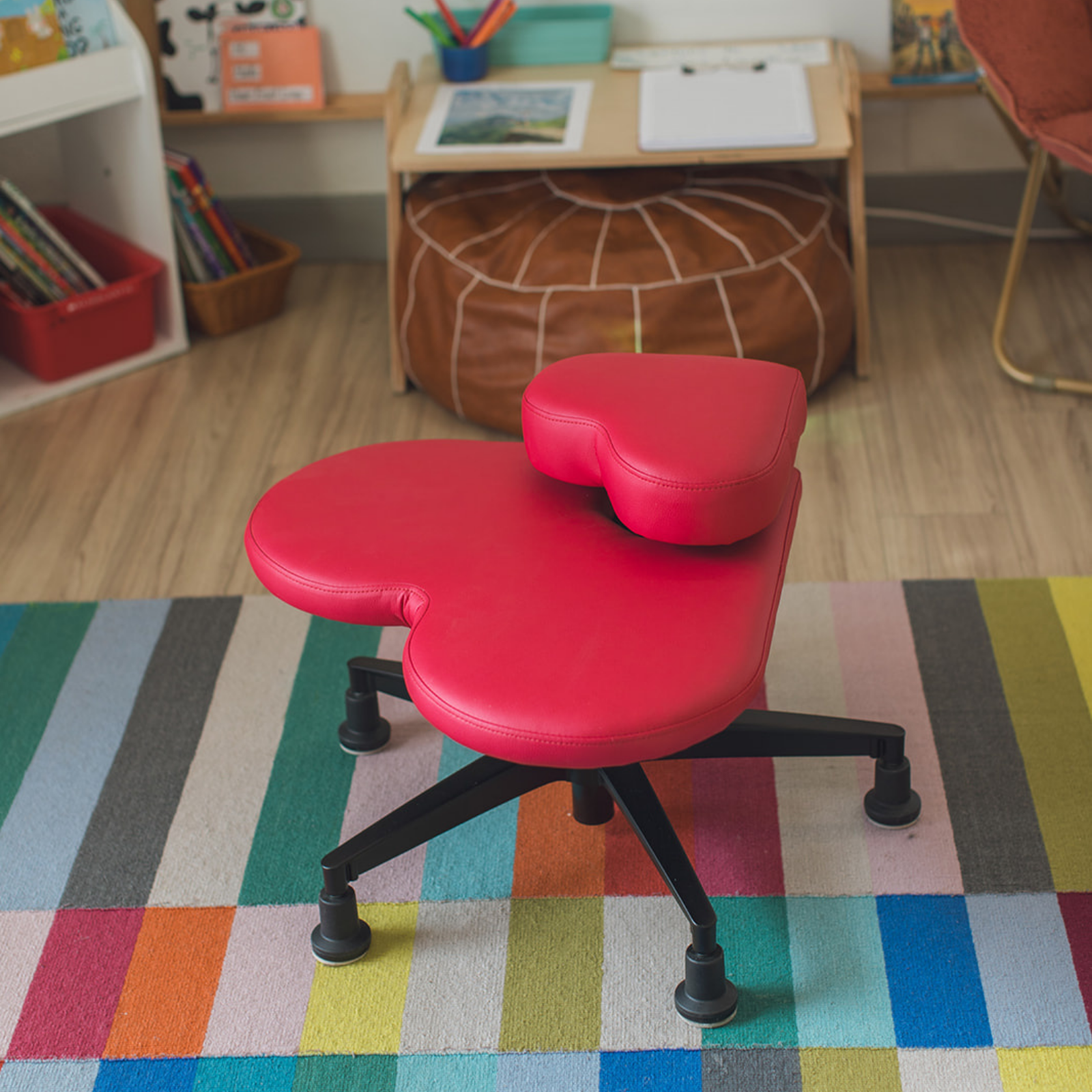 A bright red heart-shaped fidget seat for kids on a colorful striped rug in a child's classroom.